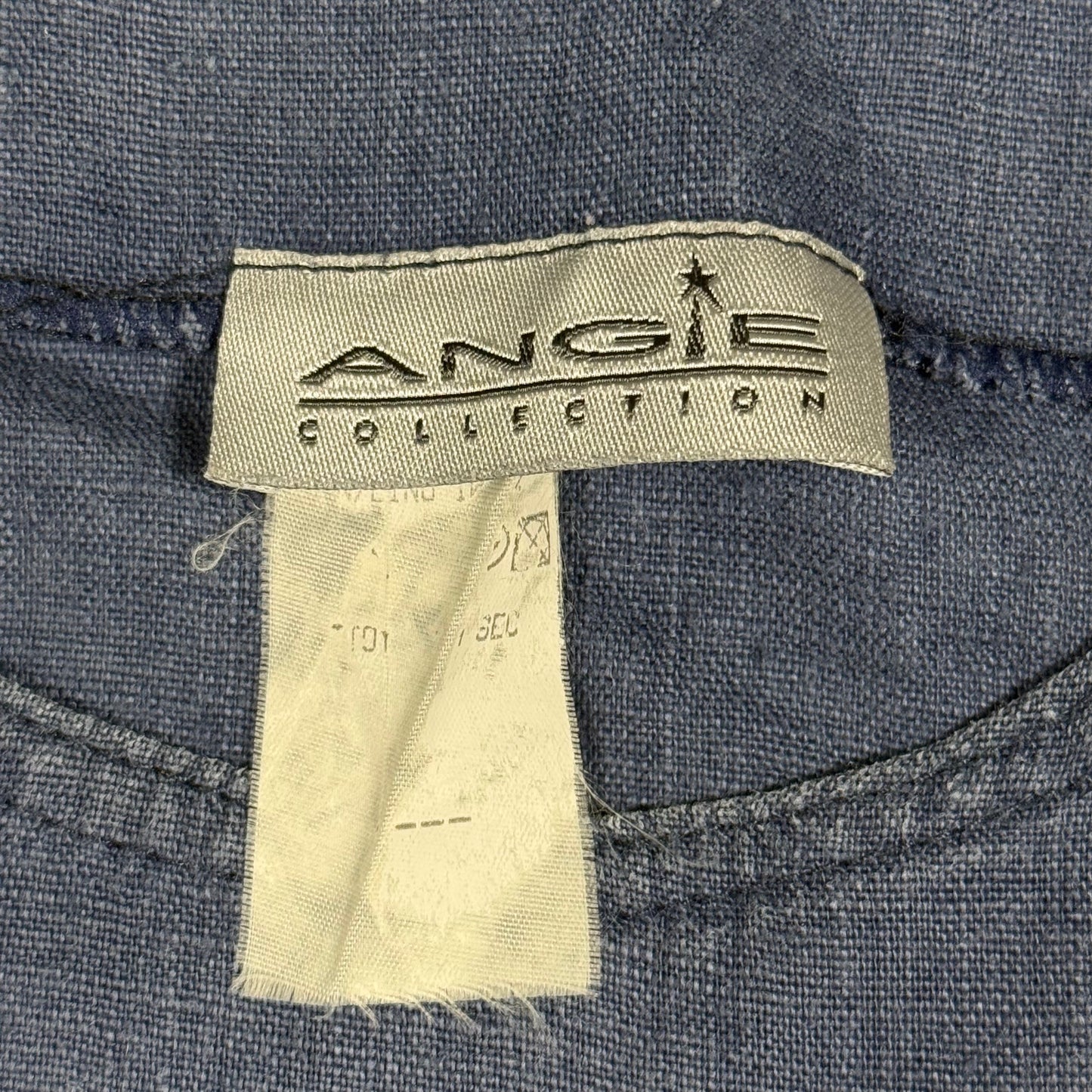 Close-up of a denim garment label reading 'ANGIE COLLECTION' stitched onto blue denim fabric, with a second off-white care tag hanging below.