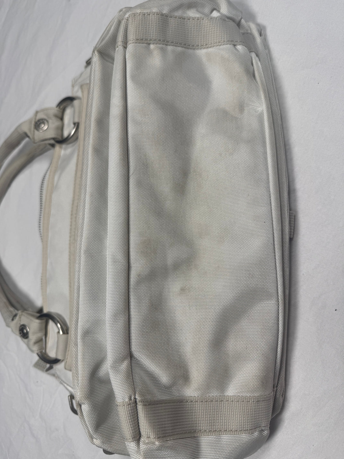 A light beige nylon shoulder bag with a top zipper, side zipper, and a shoulder strap with metal rings, shown on a white background.