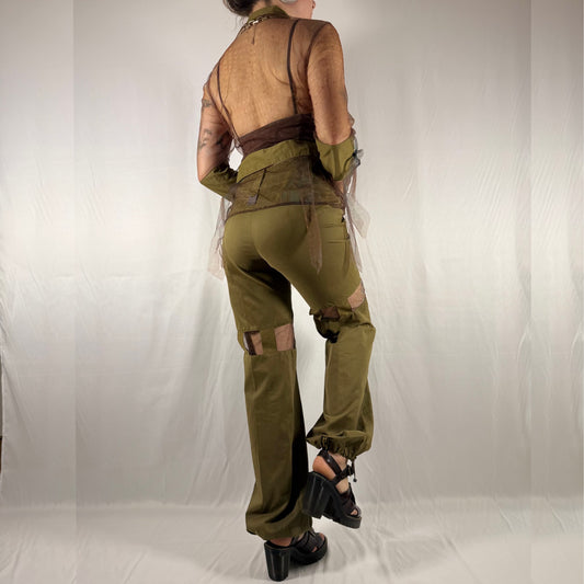 A model shown from the back wearing a vintage-style military-inspired outfit consisting of olive green cargo pants with brown knee patches, a matching olive green vest, and a sheer brown mesh top, set against a white studio backdrop.