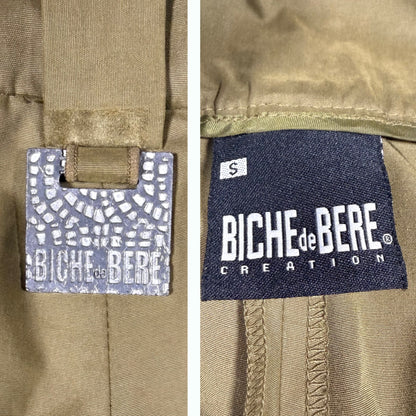 Close-up of a khaki garment showing two brand labels: a mosaic-patterned Biche de Bère tag on the left and a dark blue sewn-in Biche de Bère Creation label on the right.