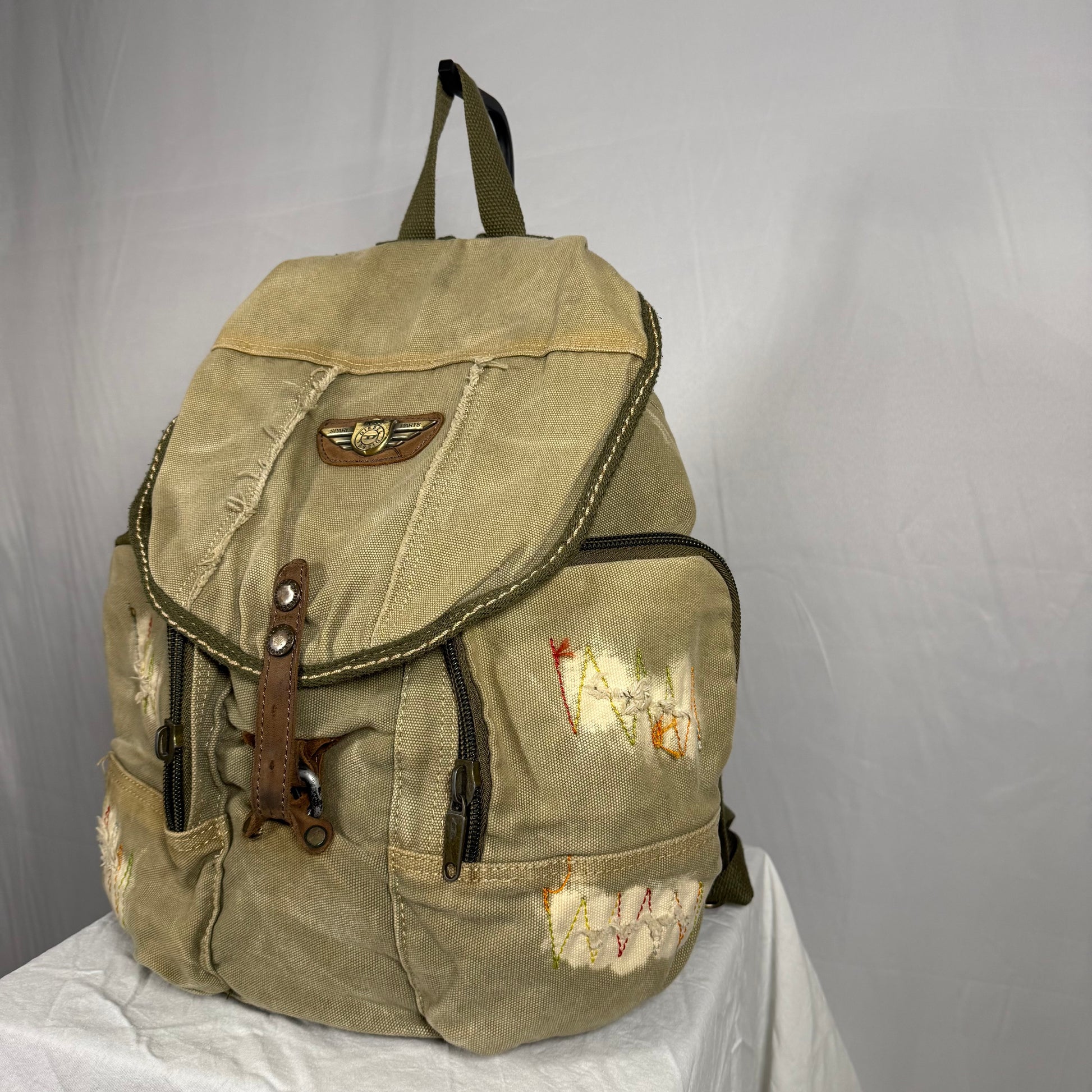 Beige backpack with patches on a white surface against a gray background