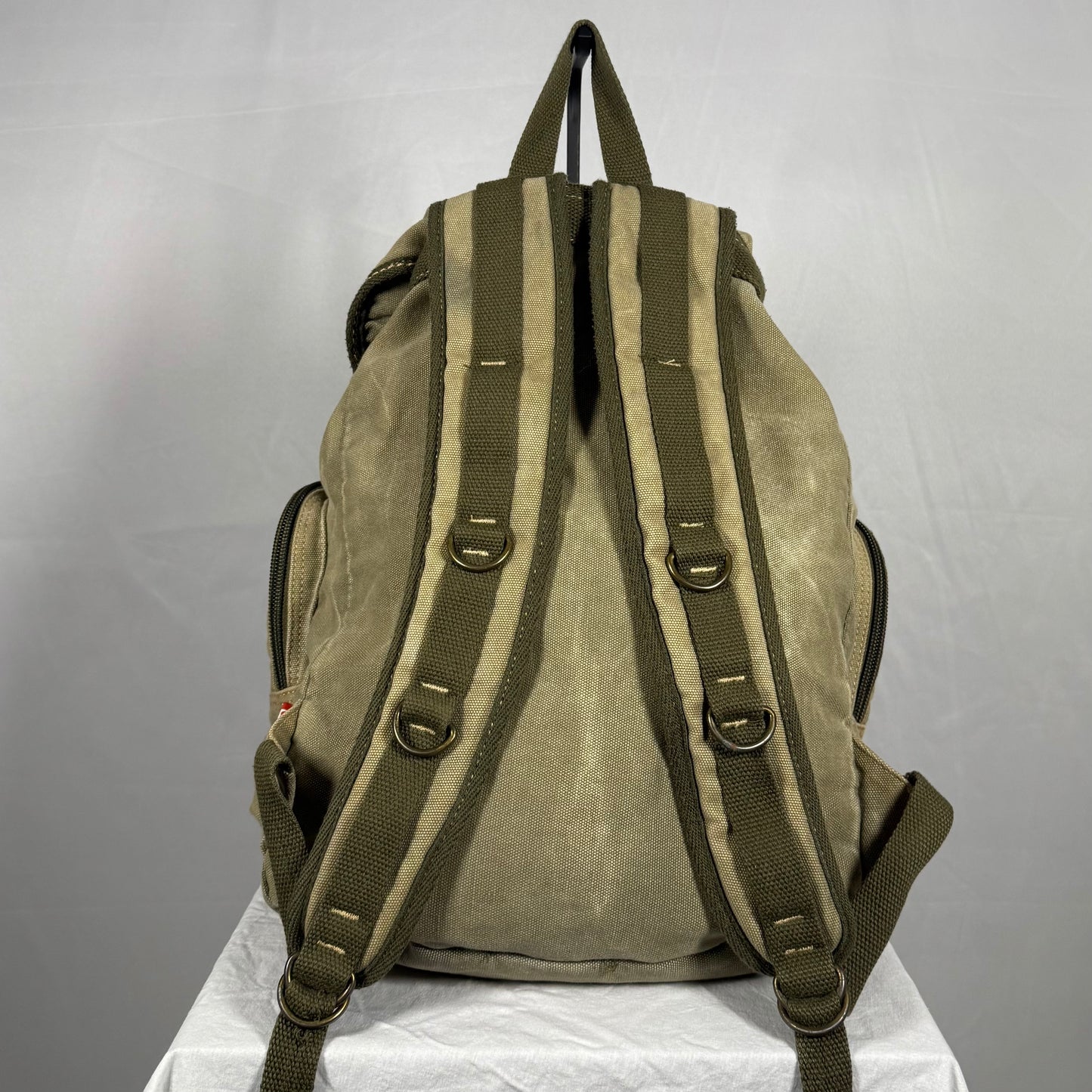 Brown backpack with green straps on a white surface against a gray background