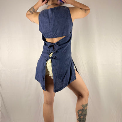 A person modeling a sleeveless blue dress from the back, showing a cutout back with lace-up detailing and a cream lace insert, against a white fabric backdrop.