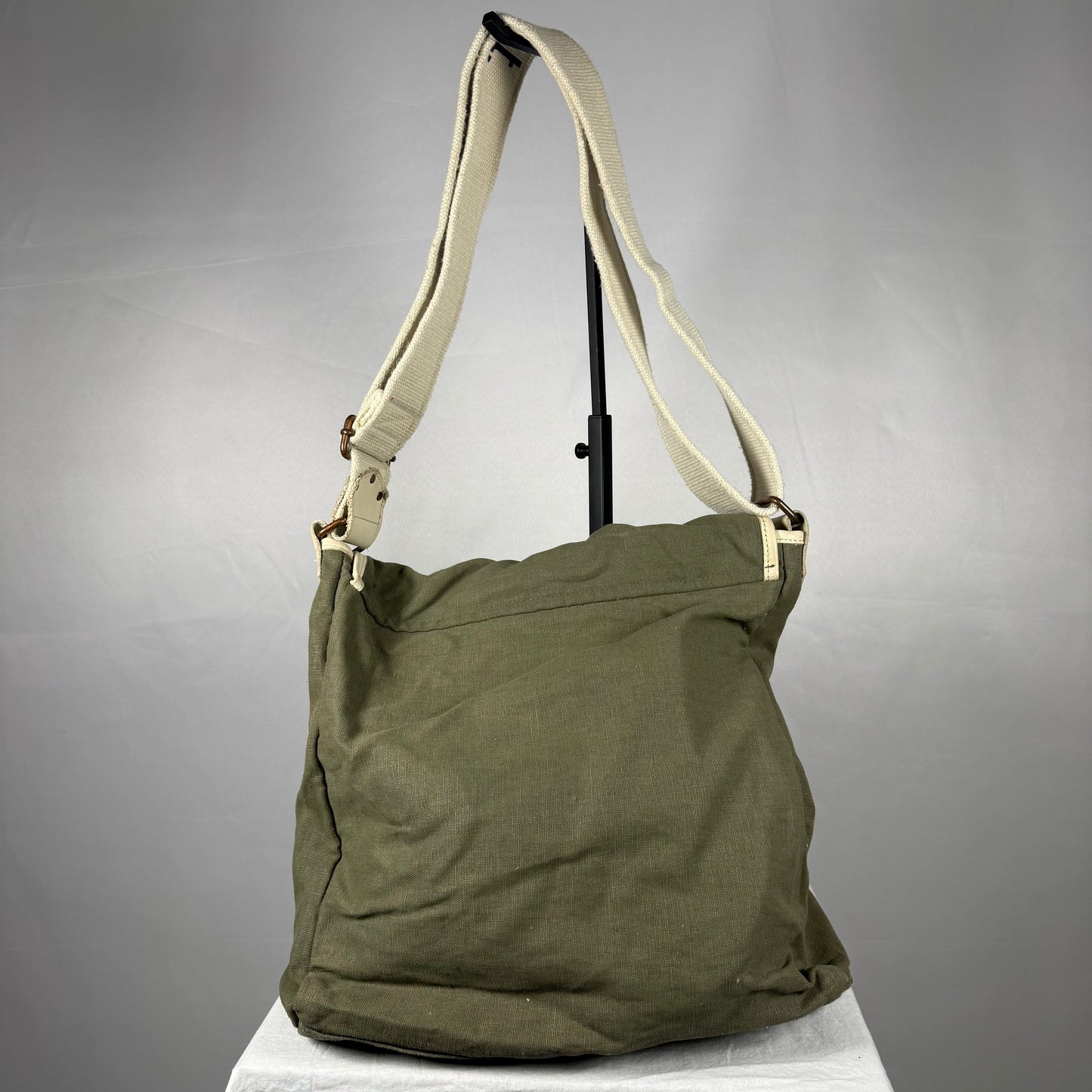 An olive green canvas shoulder bag with a beige strap, displayed on a white surface against a gray background.