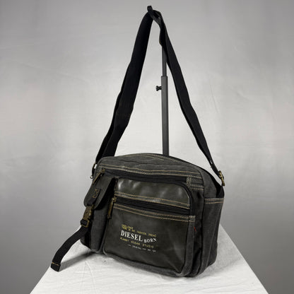 A black canvas crossbody bag with a front zippered pocket and a white printed 'DIESEL BORN' logo, displayed on a white surface against a gray background.