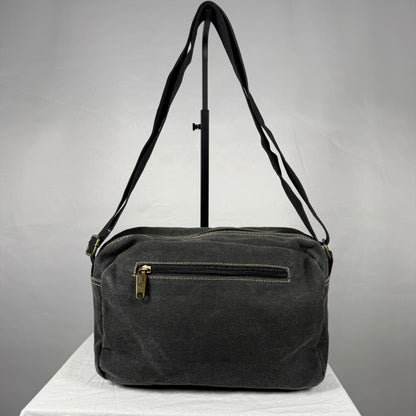A dark gray canvas shoulder bag with a front zippered pocket and a gold-tone zipper pull, displayed on a white surface against a gray background.