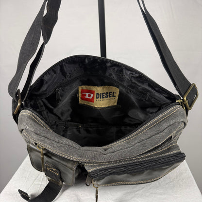 A Diesel crossbody bag shown open, featuring a gray canvas exterior, black interior lining, and brass hardware. The Diesel brand label is visible inside the bag.