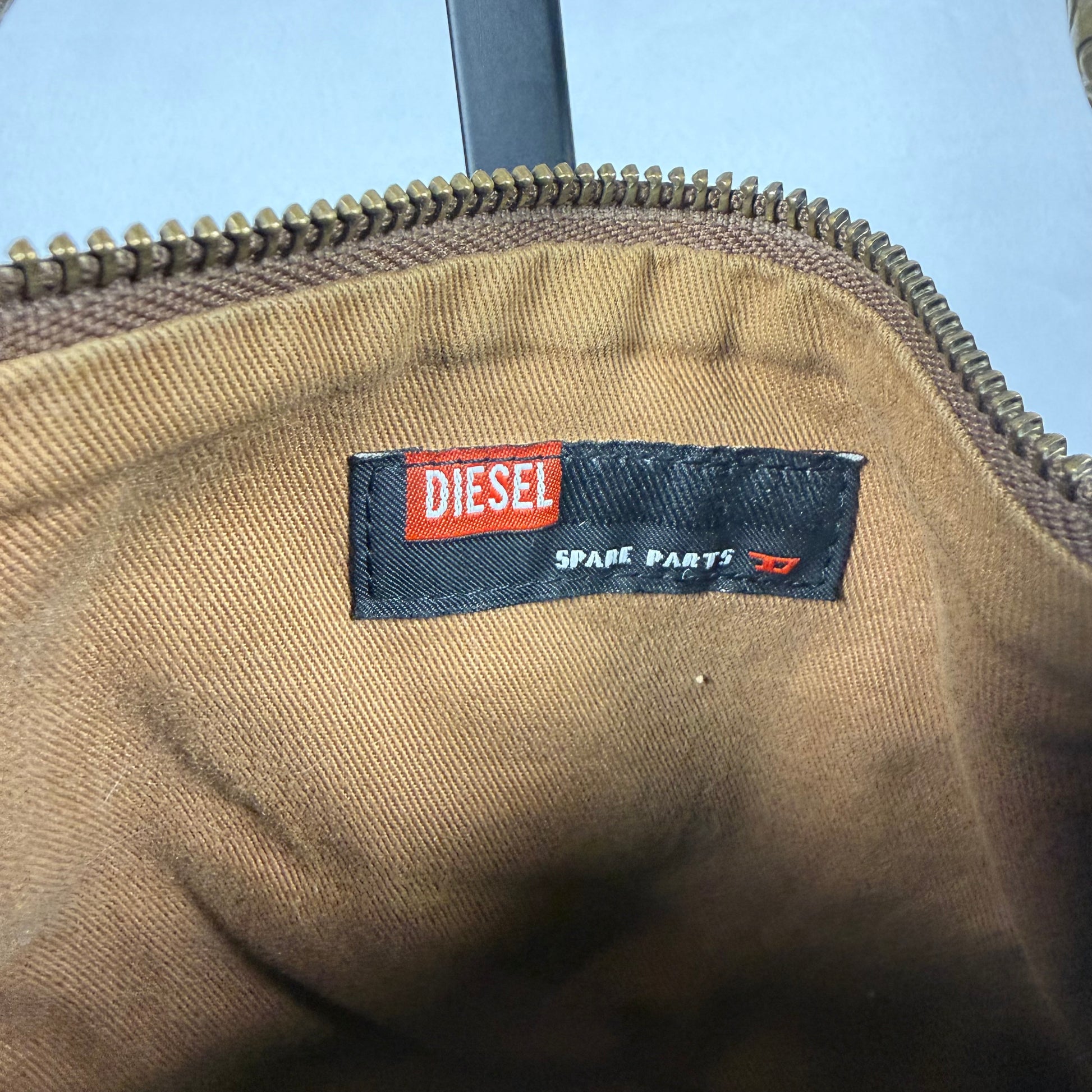 Close-up of a Diesel Spare Parts zipper pouch interior, showing the black and red brand label sewn onto a tan canvas lining.