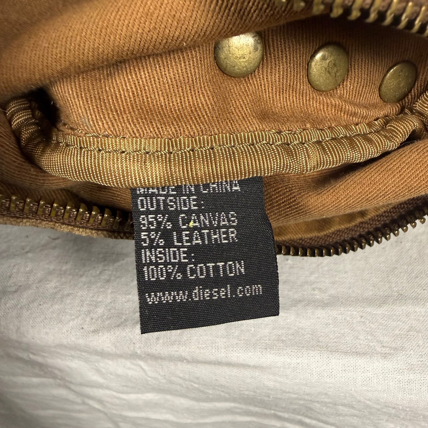 Close-up of a black fabric product tag with white text reading 'MADE IN CHINA OUTSIDE: 95% CANVAS 5% LEATHER INSIDE: 100% COTTON www.diesel.