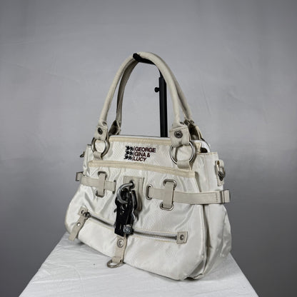 A vintage-style white nylon handbag with beige straps, silver-tone hardware, and a black embroidered patch reading 'GEORGE GINA & LUCY' on the front, displayed on a white surface against a gray background.