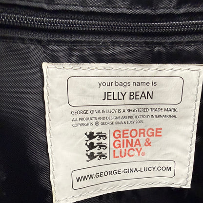 Close-up of a white sewn-in label on a black nylon bag, printed with the George Gina & Lucy brand name, website, and a customizable text field that reads 'your bags name is JELLY BEAN'.