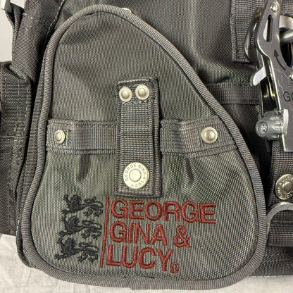 Close-up of a gray nylon utility pouch with red embroidered text reading 'GEORGE GINA & LUCY' and a black crest logo, plus silver metal snaps and clips.