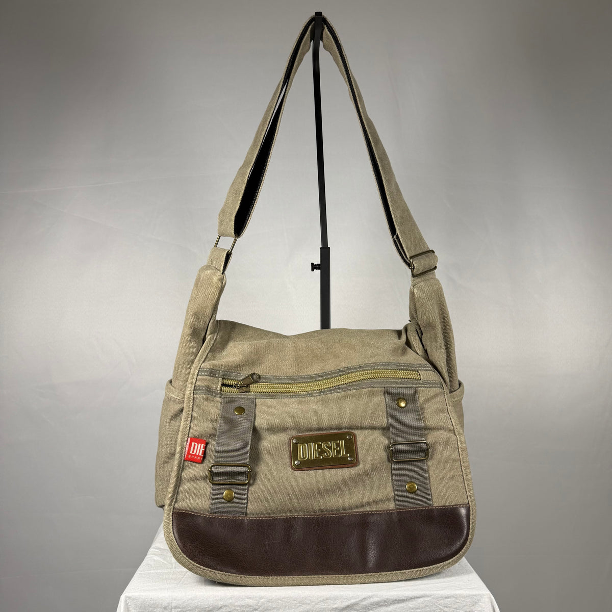 Vintage khaki Diesel messenger bag in canvas with a dark brown leather front panel, adjustable shoulder strap, metal logo plate, front pockets, and zip closure.