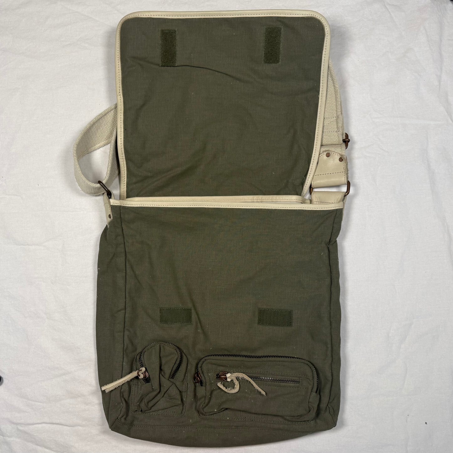 An olive green canvas messenger bag with beige trim, shown open to display its interior and multiple exterior pockets, laid flat on a white fabric background.